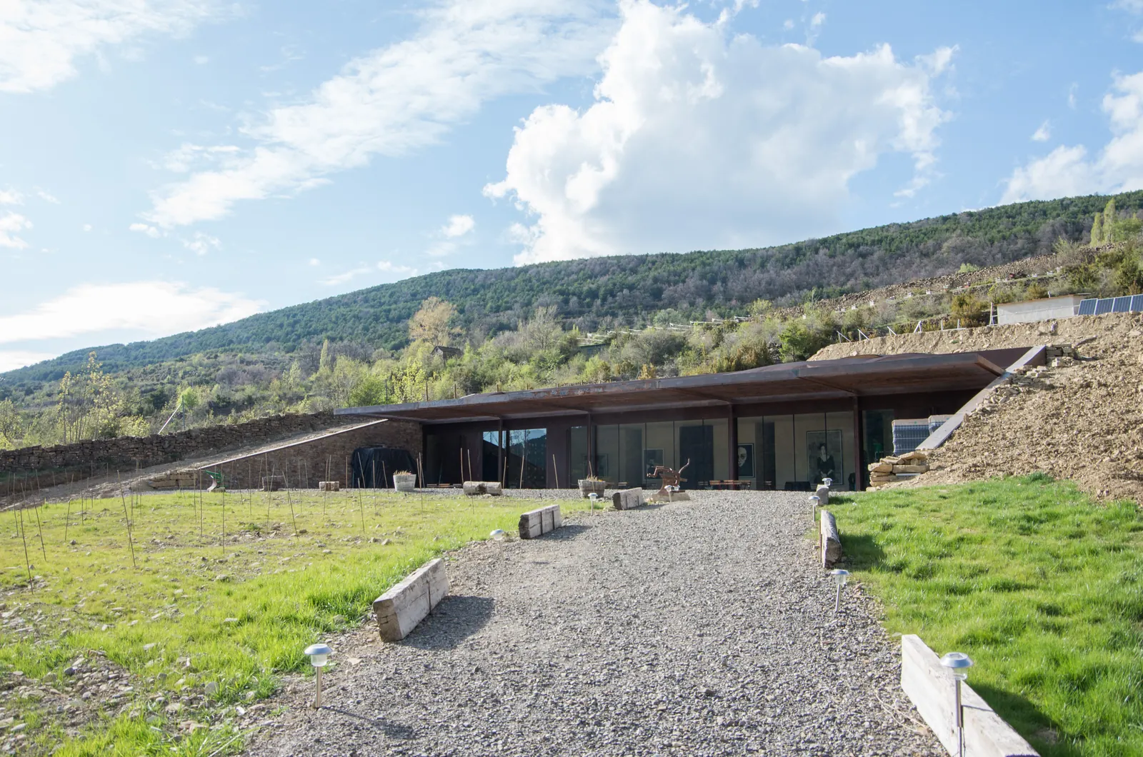 La bodega de Bal Minuta, baja y metida en la ladera de Barbenuta, con el camino de grava y el monte detrás, en el Valle de Tena